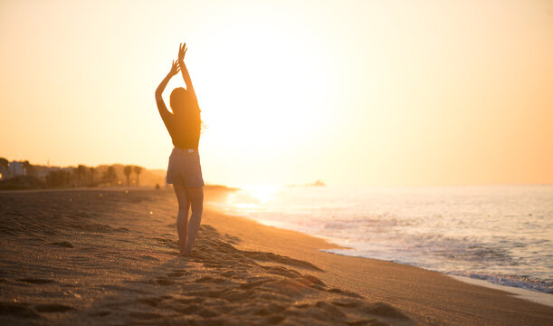Beauty young happy woman raising hands, sea side. Girl's silhouette on a summer beach over sunrise. Beautiful woman enjoying nature in sunlight. Sunset. Healthy lifestyle, vacation, happiness concept