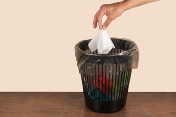 Man putting paper tissue into trash bin on light brown background