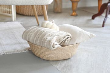 Folded knitted beige linen blanket and pillow inside a rustic woven backet. Wicker basket with cozy plaid. Home interior