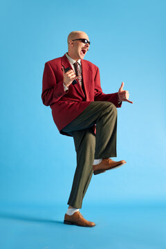 Full lenght image. Balded man with mustache dressed vintage dansing with call-sign and shouting over blue background.