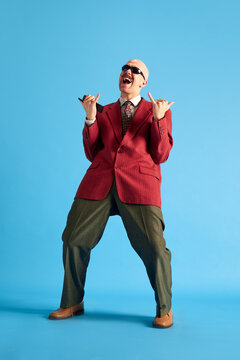 Full lenght image. Balded man with mustache dressed vintage dansing with call-sign and shouting over blue background.