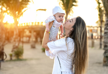 Obraz premium Side view of mother hugging her baby boy at sunset. Concept of union and tender connection between a young mama and his lovely child.