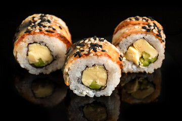 Close-up of sushi rolls with tuna, cucumber and avocado on a black background.