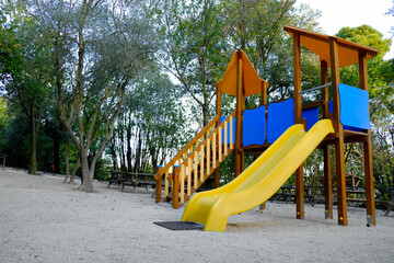 Empty playground with beautiful slide, benches and trees in park. Space for text