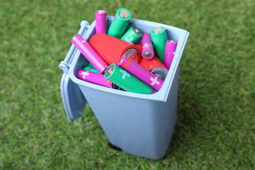 Many used batteries in recycling bin on green grass