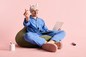 Image of man sitting on bag chair in pajama and funny headband with laptop with love-sign over...