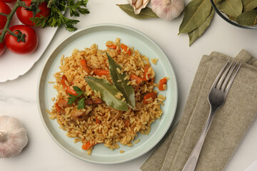 Delicious pilaf, bay leaves, ingredients and fork on white table, flat lay