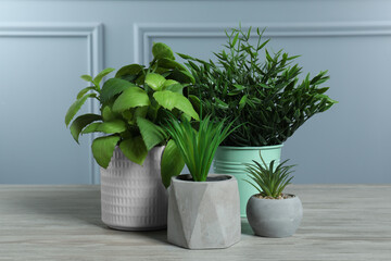 Many different artificial plants in flower pots on white wooden table near grey wall