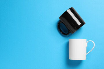 White and black ceramic mugs on light blue background, flat lay. Space for text