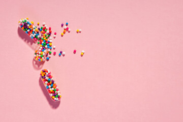 Medical pill capsules filled with colorful sugar sprinkles on pink background. Creative concept