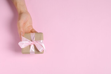 Man holding gift box with bow on pink background, top view. Space for text