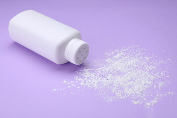 Bottle and scattered dusting powder on violet background. Baby cosmetic product