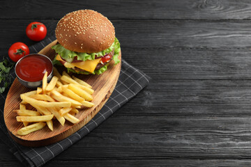 Delicious burger with beef patty, tomato sauce and french fries on black wooden table, above view....