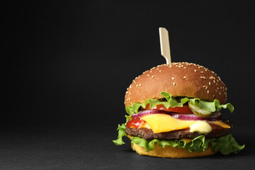 Delicious burger with beef patty and lettuce on black background, space for text