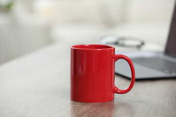 Red ceramic mug and laptop on wooden table indoors