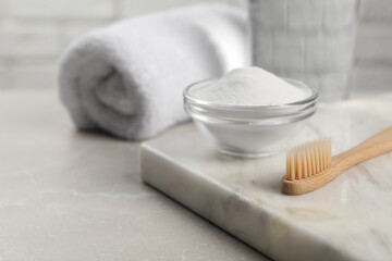 Bamboo toothbrush and glass bowl of baking soda on light table, space for text