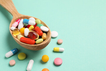 Wooden spoon with many different pills on turquoise background, closeup. Space for text