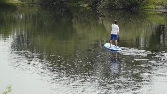 caucasian man on supboard. a man with glasses stands and rows with an oar on the board. the man swims to the other side of the pond. water sports. High quality Full HD video recording