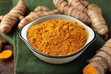 Bowl with aromatic turmeric powder and raw roots on table, closeup