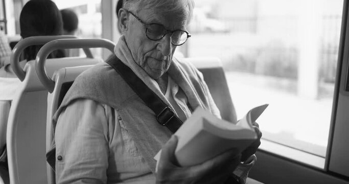 Senior man sitting inside tram while reading a book - Elderly person traveling - Black and white editing 