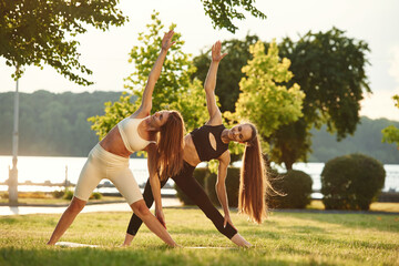 Two women in sport clothes are doing exercises outdoors on the field