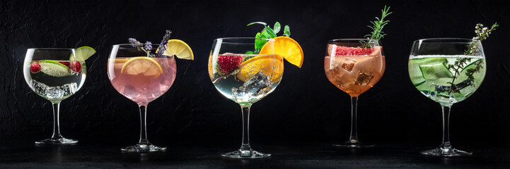 Fancy cocktails variety with fresh fruit. Many gin and tonic drinks with ice at a party, panorama on a black background - obrazy, fototapety, plakaty