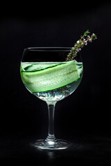 Fresh cocktail. Gin and tonic drink with ice at a party, on a black background. Alcohol with cucumber and thyme
