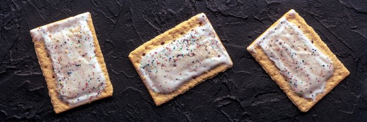 Pop tarts panorama. Poptart toaster pastry with icing on a black slate background, overhead flat...