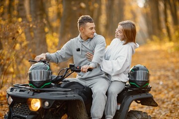 Man and woman hugging on a quad bike in autumn forest