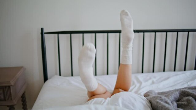 Carefree woman legs moving bedroom background. Unrecognizable girl lying on bed