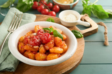 Potato gnocchi. Traditional homemade potato gnocchi with tomato sauce, basil and parmesan cheese on turquoise rustic kitchen table background. Traditional Italian food. Top view.