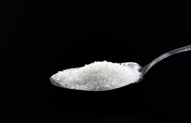 A small teaspoon with sugar, on a black background.