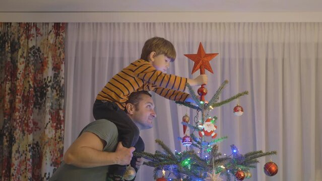 Little boy on father's shoulders put the star on top of Christmas tree