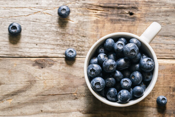 Fresh raw organic farm blueberry in white cup on rustic wooden background.