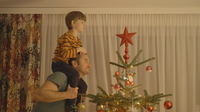Father with piggyback son putting the star decoration on top of Christmas tree