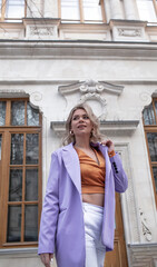 A beautiful fashionable girl walks through the streets of the city, The woman is wearing white jeans,  a yellow top and lavender-coloured jacket