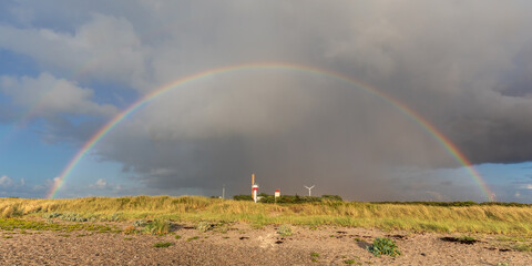 Fototapeta na wymiar Himmel mit Regenwolken und Regenbogen über dem Strand der Ostsee auf Fehmarn in Schleswig-Holstein. Unter dem Regenbogen der Leuchtturm Westermarkelsdorf