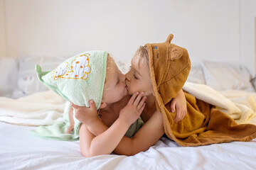 Two cute blond beautiful children, boy and girl, lying on the bed after bath, cuddling