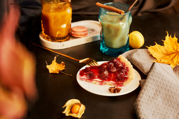 Atmospheric glass of pumpkin latte, cinnamon sticks and cherry pie. Seasonal autumn coffee time. Cozy home aesthetic
