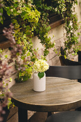 Tables and chairs on the cafe's summer terrace with climbing plants on the wall and hydrangea flowers on the tables.