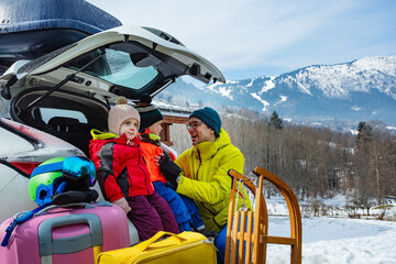Dad help dress kids sitting in car trunk over snow mountain