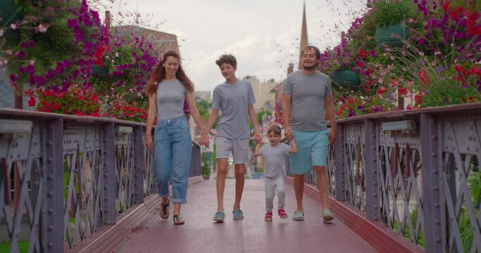A large family of four are walking through a colorful park. A family with children of three and thirteen years old spend time together on the street of a big city in Europe