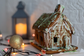 handmade gingerbread house with glaze standing on table with tablecloth and decorations. Holiday mood