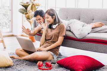 Young couple relaxing and smiling on a couch at home and making a video call to friends. Asian...