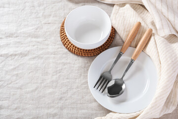White plate and bowl with spoon and fork  with linen napkin on tablecloth background