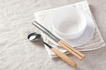 White plate and bowl with chopsticks and spoon on linen napkin, table setting