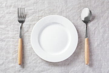 White plate with fork and knife on linen tablecloth, table setting