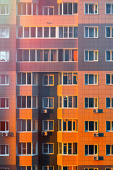 Fototapeta na wymiar Dramatic view of the facade of a multi-storey residential building at sunset. Ominous red reflections of the sun behind the building.