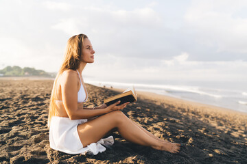 Dreamy woman reading book on seashore