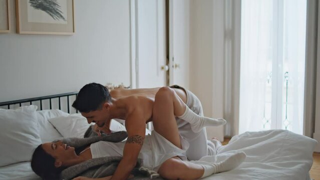 Excited man jumping on bed mattress. Joyful lovers playing at morning bedroom